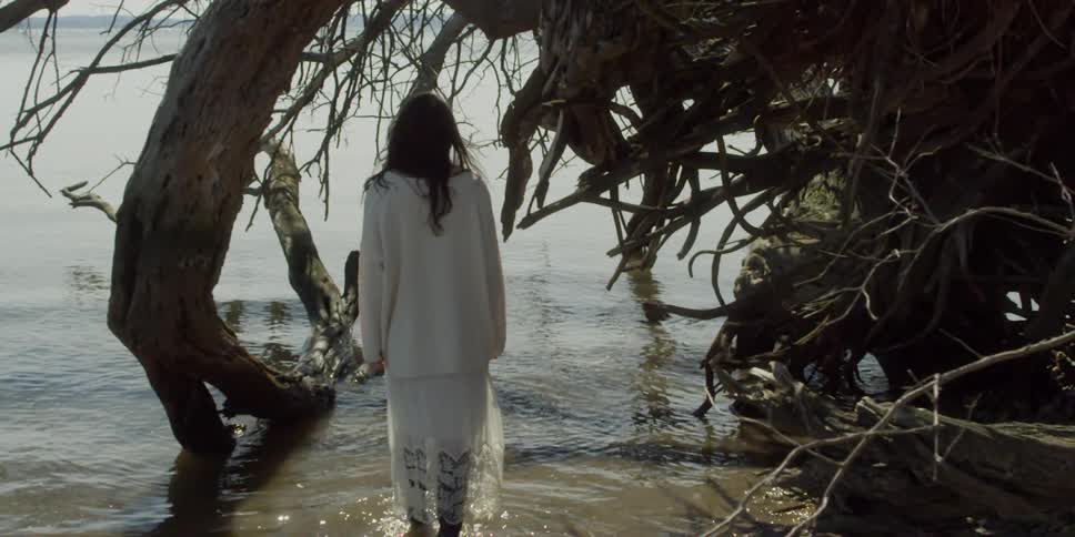 A woman stands by a tree in the shore
