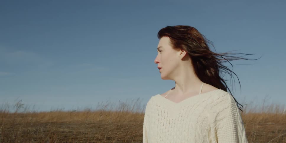 A woman stands in a windy field on a sunny day