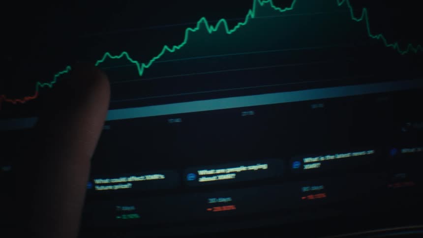 A digital screen likely a smartphone or tablet displaying a financial tracking interface in a dark environment two primary lines are visible on the interfacethe most prominent line is a jagged bright green trend line that tracks the price or value