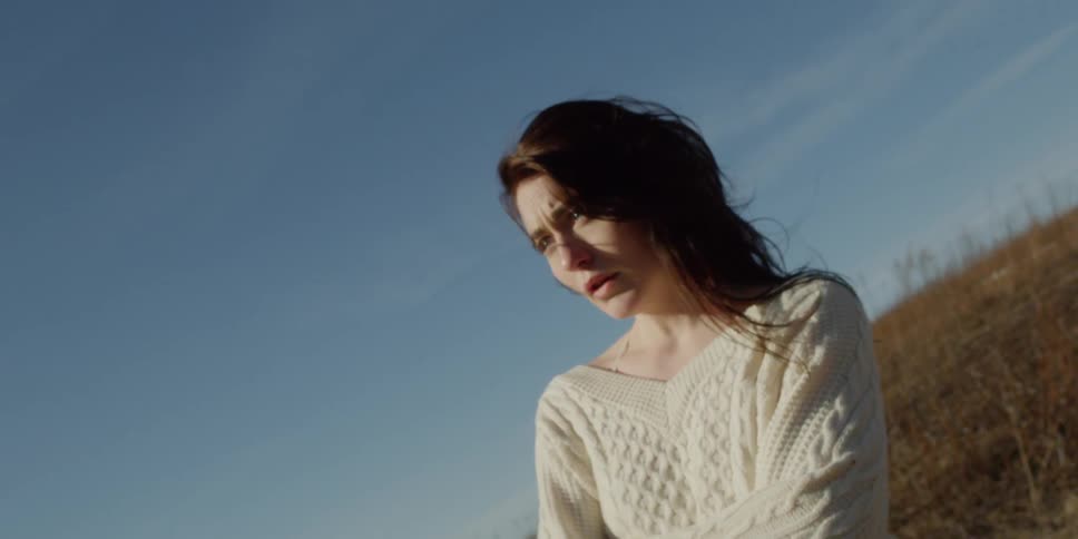 A woman stands in a field on a sunny and breezy day