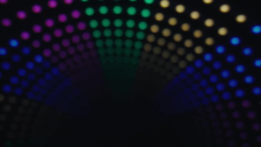 An abstract pattern of blurred multicolored lights creates a symmetrical tunnel effect against a dark background