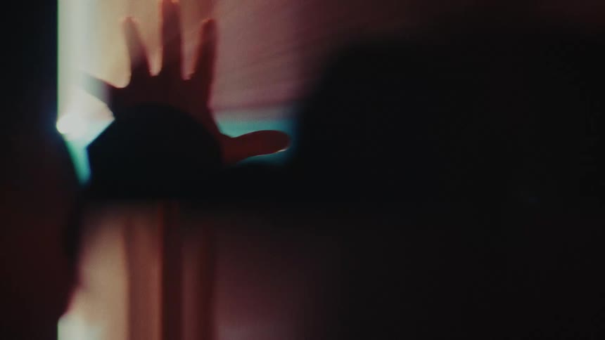 A hand reaches toward a bright cinematic light source that creates dramatic lens flares and hazy reflections warm orange and cool blue tones wash over the scene as the silhouette interacts with the glowing projection