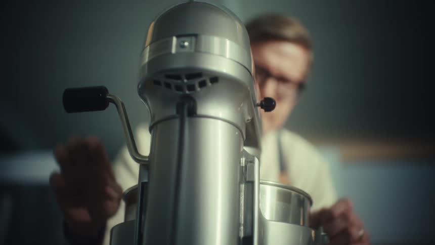 A person operating a silver stand mixer from a rear perspective in a kitchen environment