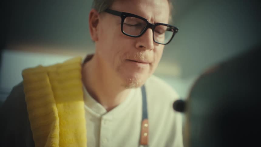 A middleaged man in the kitchen watching a mixer mix dough wearing glasses at midday