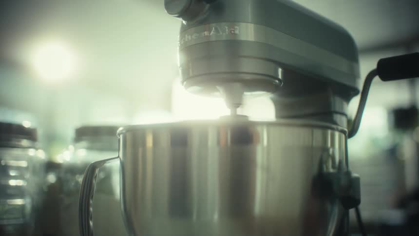 A silver stand mixer sits on a kitchen counter with baking ingredients under soft bright lighting