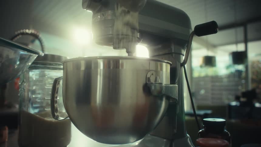 Granulated sugar falls into a mixer bowl during dough preparation