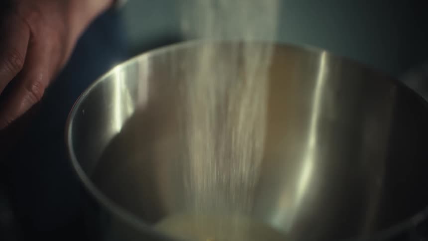 The man pours an ingredient into the bowl