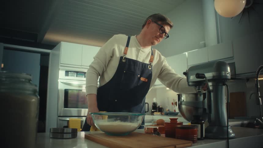 A man wearing an apron uses a silver stand mixer to prepare food in a modern kitchen