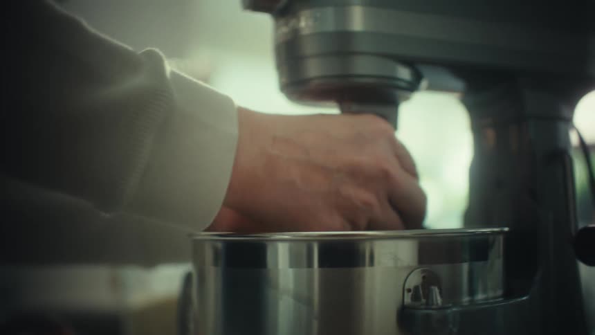 Hand adjusts mixer bowl during dough preparation