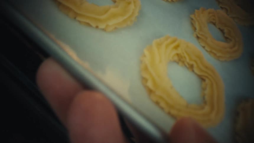 A baker slides a tray of shaped cookie dough onto the center rack of a dark oven