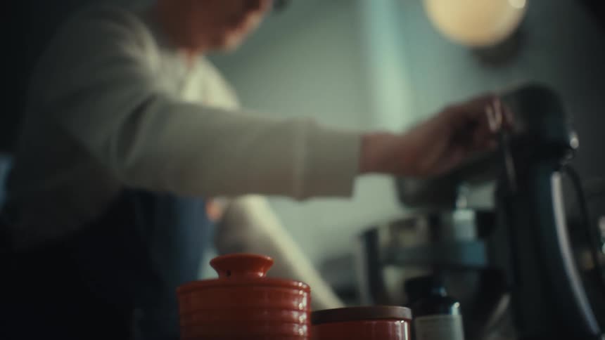 A male baker wearing glasses operating a silver stand mixer in a modern kitchen