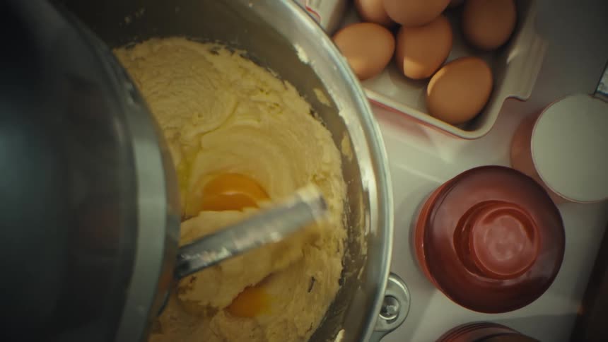 Egg is added to batter inside a mixer bowl in the kitchen