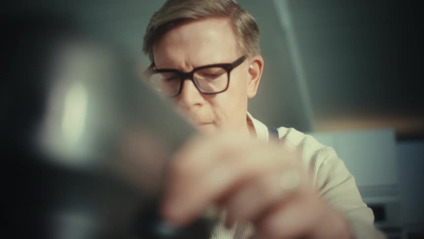 Man wearing glasses and an apron observes a kitchen mixer while dough is being prepared
