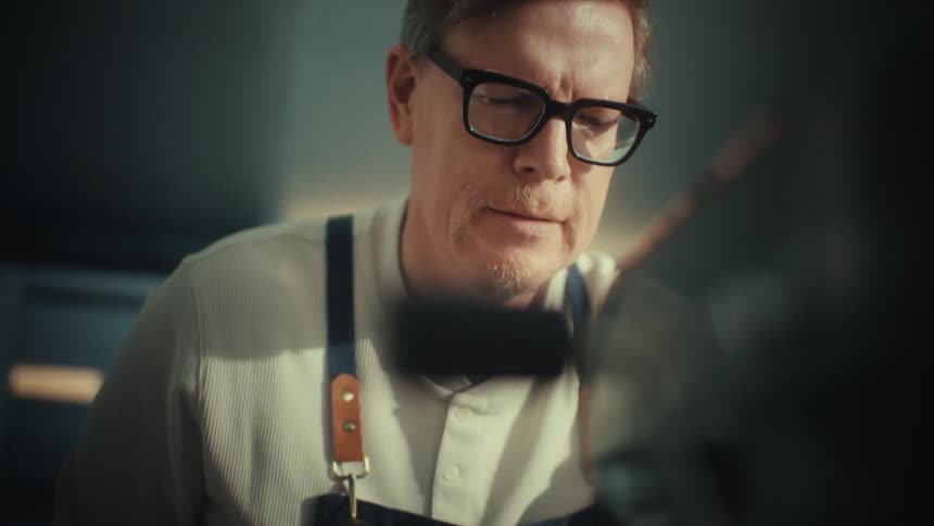 Man wearing glasses and an apron observes mixture in a kitchen mixer