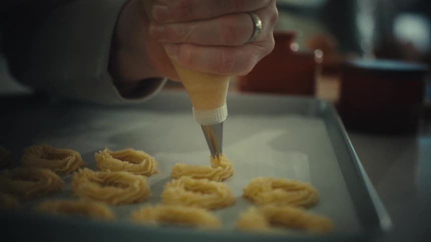 Piping bag deposits dough forming rings on a tray