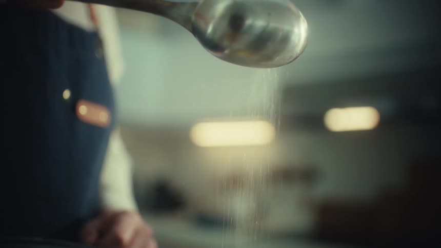 Spoon pours granulated sugar onto a surface during food preparation