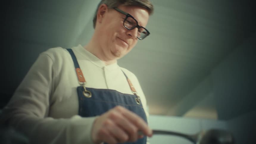 Man wearing glasses and apron stirs mixture with a spoon in a container