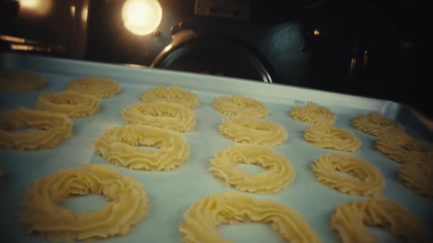 Hand places a tray with dough rings inside a heated oven