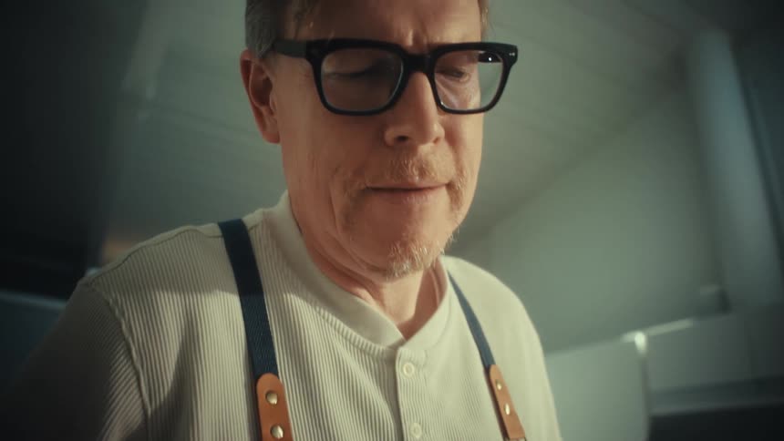 A middleaged man wearing glasses mixing flour in a bowl in the kitchen at midday
