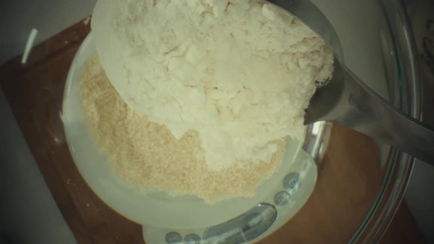 Flour is poured from a container onto a kitchen scale