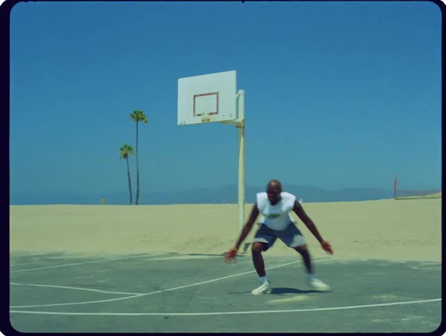 A man plays basketball on an outdoor court situated next to a sandy beach