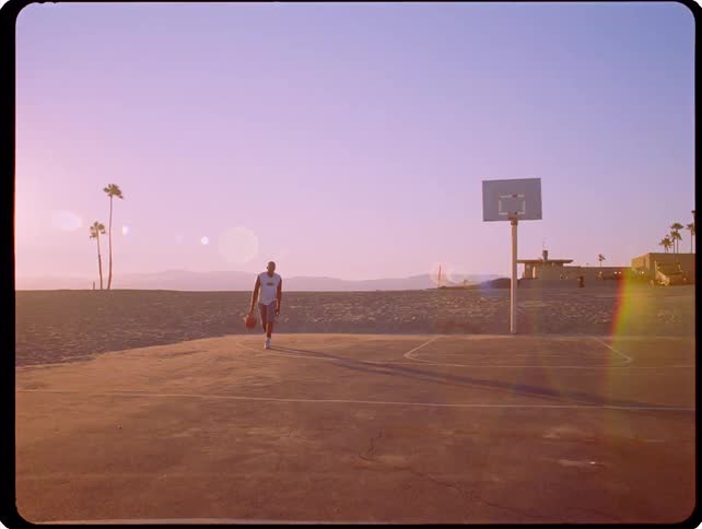 Man dribbles on a court near the beach as another man stands nearby in summer