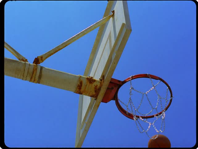 A low angle shot of a basketball dropping through a hoop and net against a clear blue sky