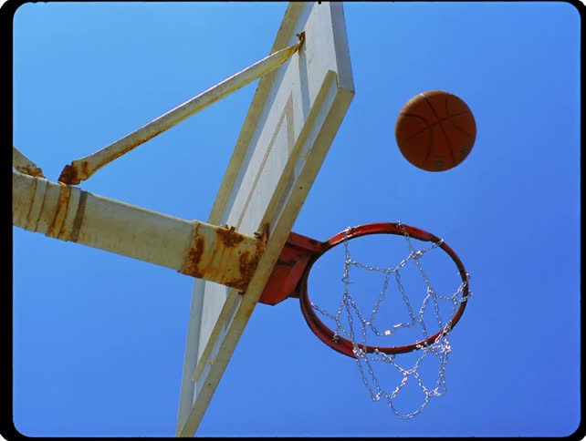 A basketball bounces off the rim of an outdoor hoop with a chain net under a clear blue sky