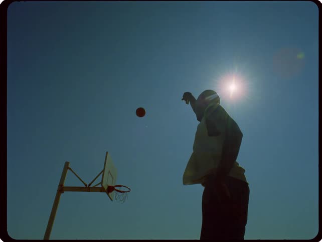 A male athlete throws a basketball toward the hoop on a basketball court at sunset
