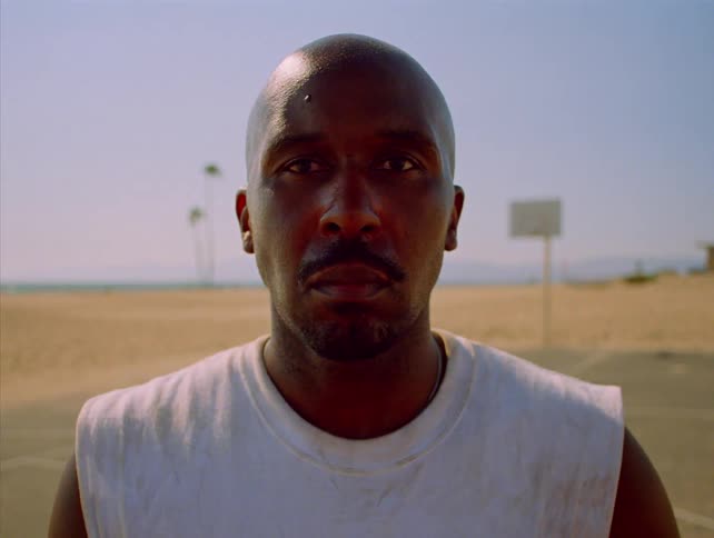 Man wearing a sleeveless shirt looks forward on a court near the beach