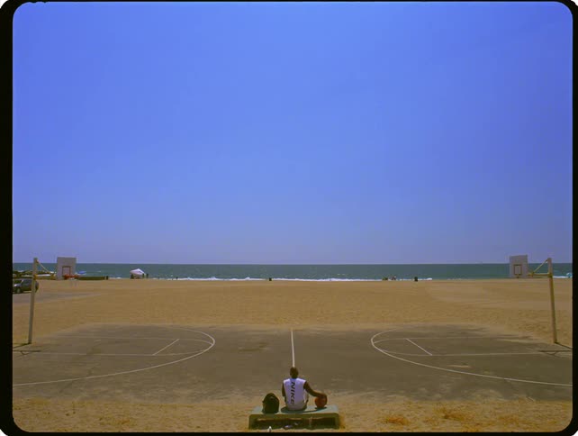 Person sitting between two beachside basketball courts looking toward the ocean