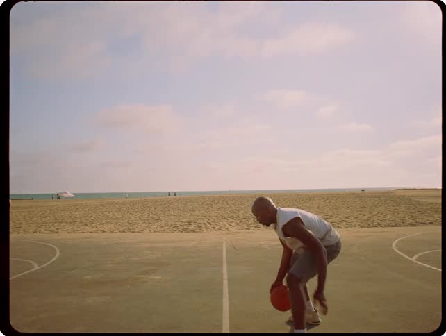 The man is dribbling a basketball on the beach court