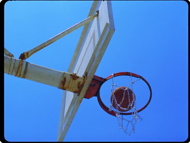 A basketball drops through the hoop against a clear blue sky