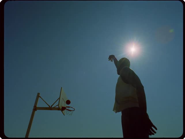 A young male athlete throws a basketball into the hoop on a basketball court at sunset