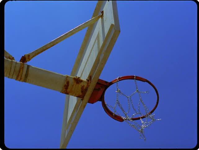 A basketball swishes through a chain net and drops out of frame before bouncing back into view just as a man briefly enters the shot to retrieve it while looking down