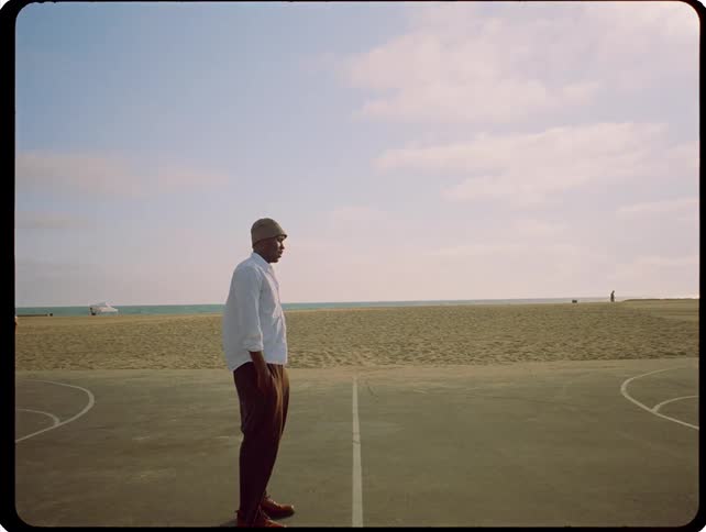 A man stands on an outdoor basketball court near the beach