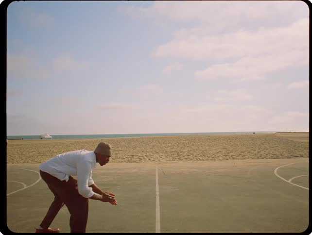 Man bends over on a beach side basketball court while clapping on a cloudy autumn day