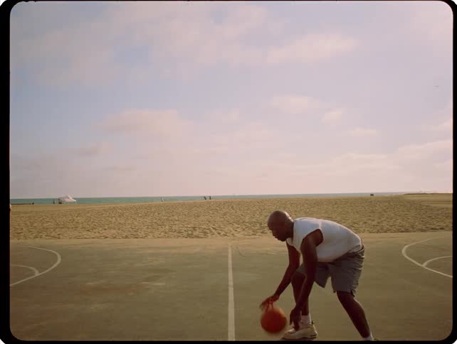 A basketball player on a basketball court juggling the basketball at midday
