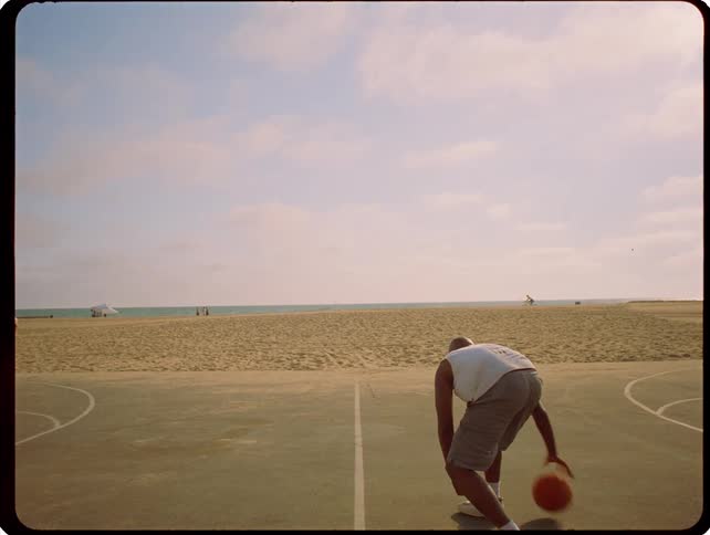A man dribbles a basketball on an outdoor court near the beach