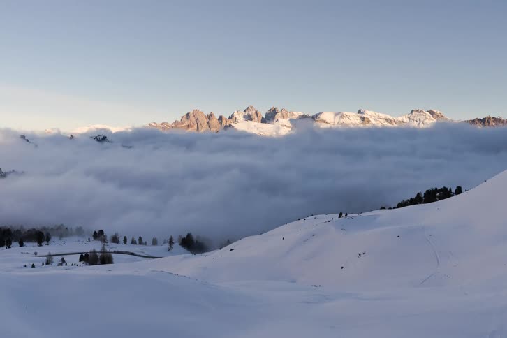 Snowcovered mountains rise above a layer of clouds under a clear sky