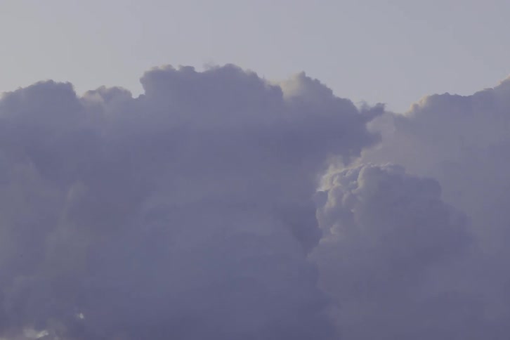 In this dramatic timelapse towering cumulus clouds churn and swell against a pale sky their edges catching the golden glow of the sun before fading into a dense hazy overcast