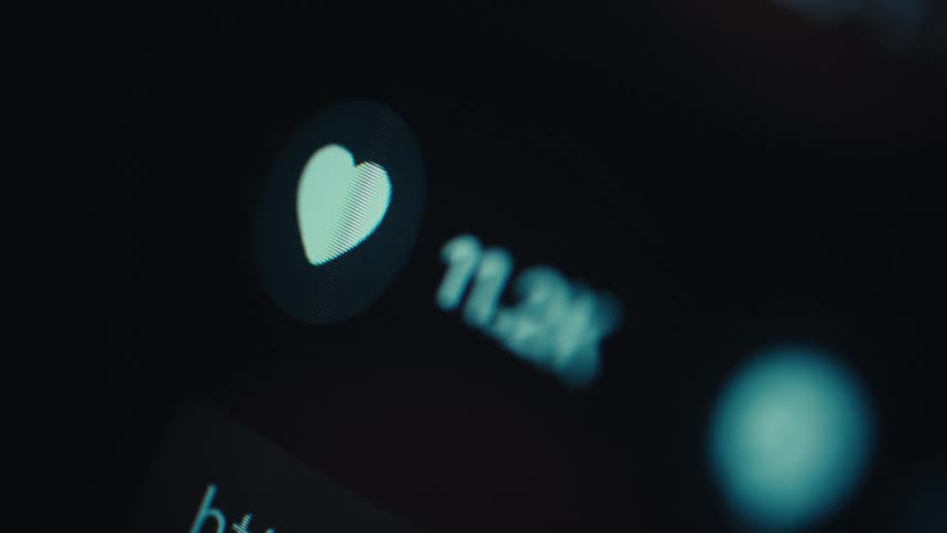 A closeup outoffocus shot of a smartphone screen shows a glowing heartshaped like icon digits changing and blurred interface elements against a dark background