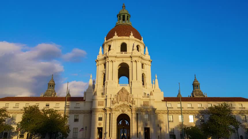 Central dome of pasadena city hall lit by sunlight with parked cars along the front avenue