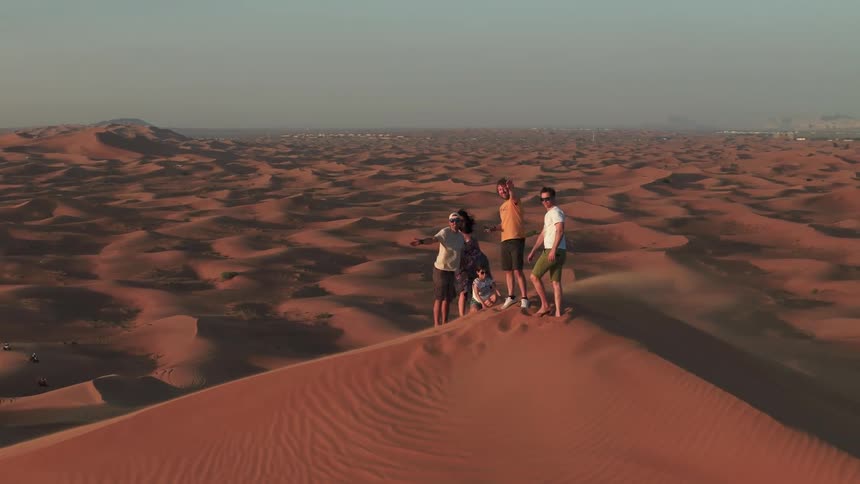 Group of people standing on top of a sand dune with vast desert surrounding them