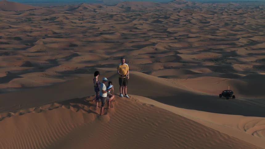 Group of people standing and sitting on top of a dune observing a landscape of desert dunes