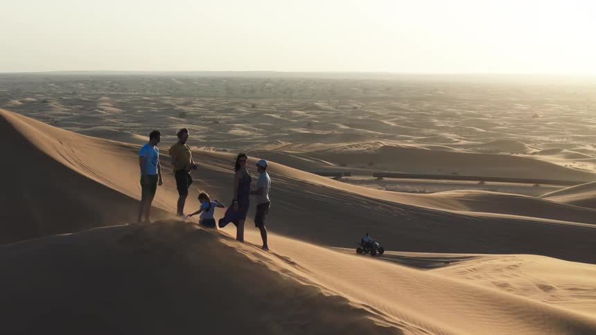 Group of people on top of a dune observing the landscape of desert dunes at sunset