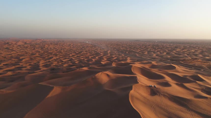 Extensive sand dunes form a desert landscape with tracks and vehicles visible in the distance