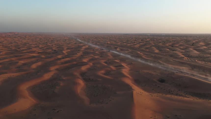 Highway passes between the dunes in a vast desert as the sun sits on the horizon
