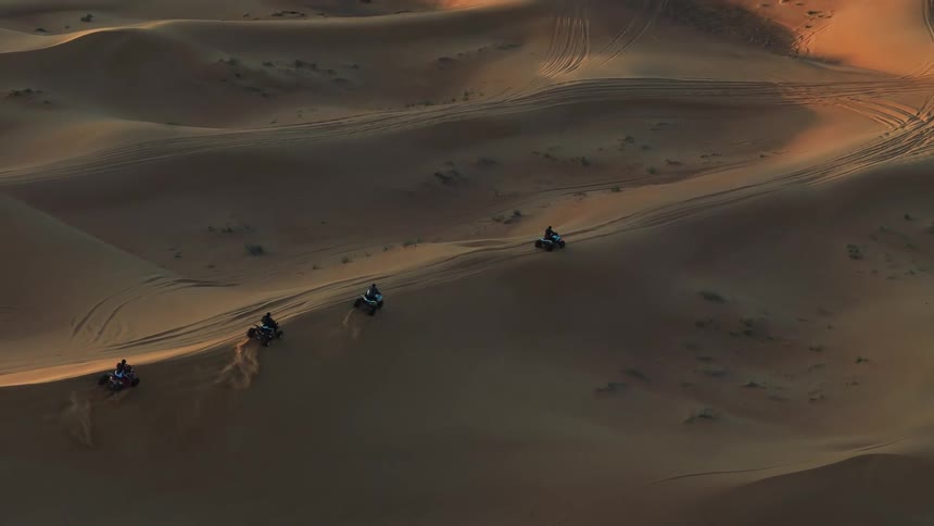 Four people ride a four wheeler over the dunes in the desert during the daytime