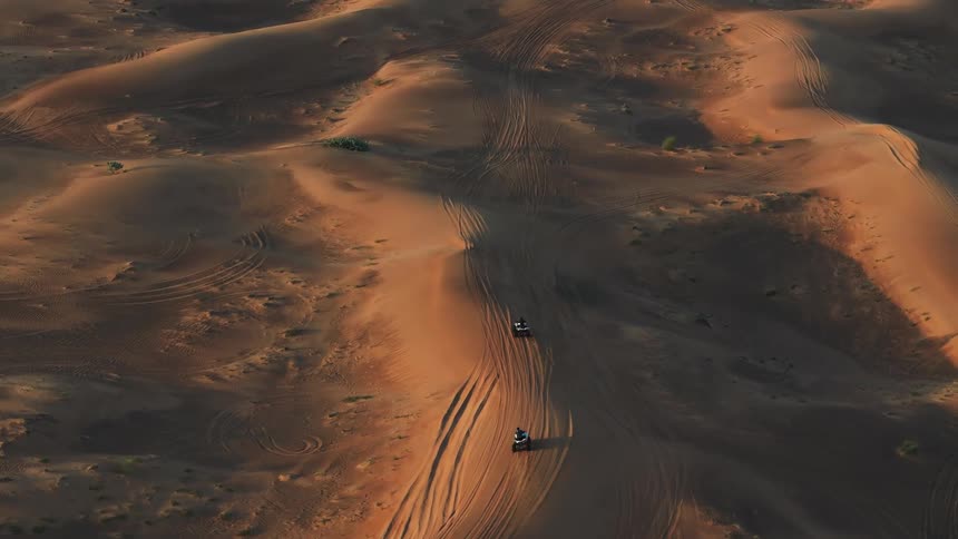 Allterrain quad vehicles travel across sand dunes leaving tracks in the desert